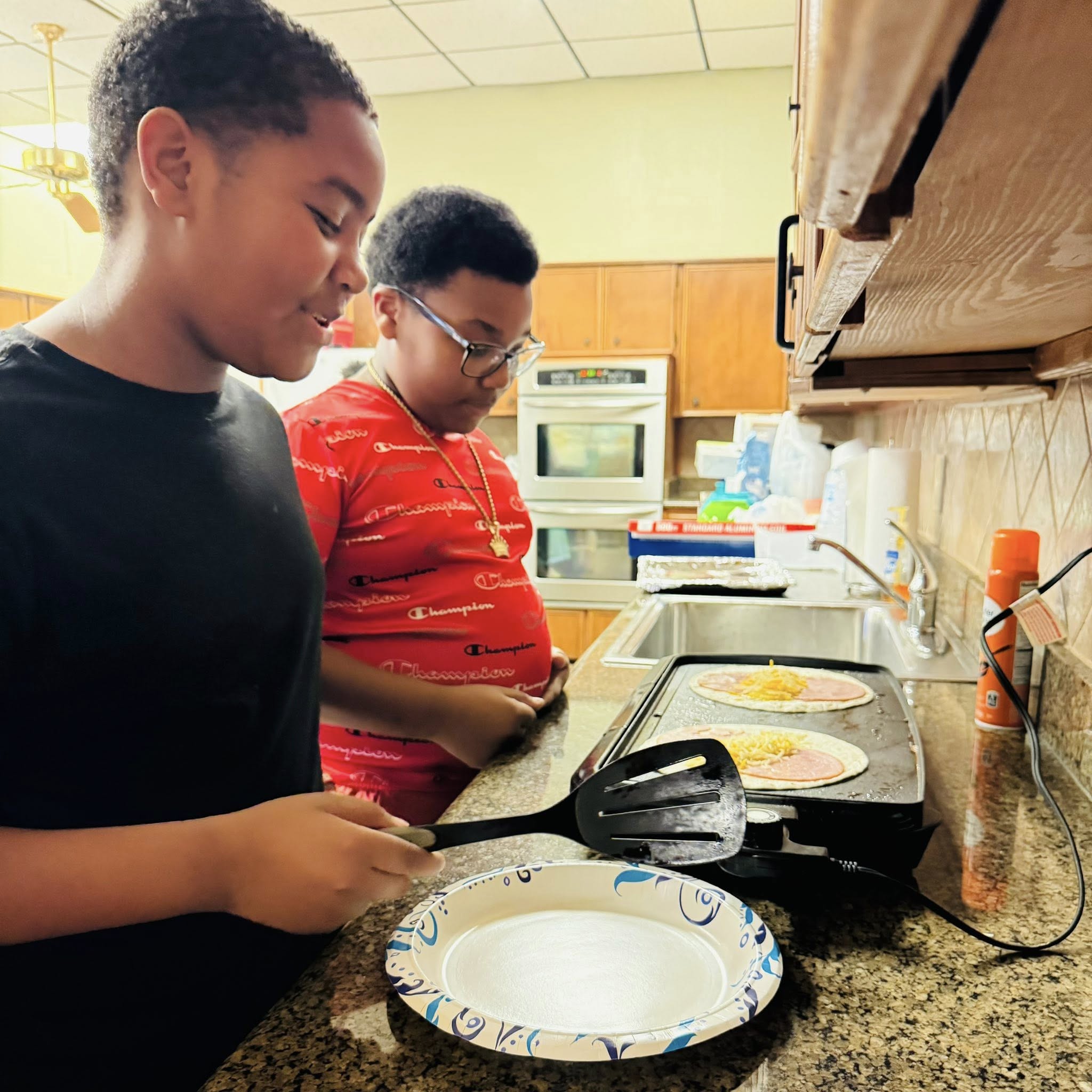 Two boys cooking on a griddle.